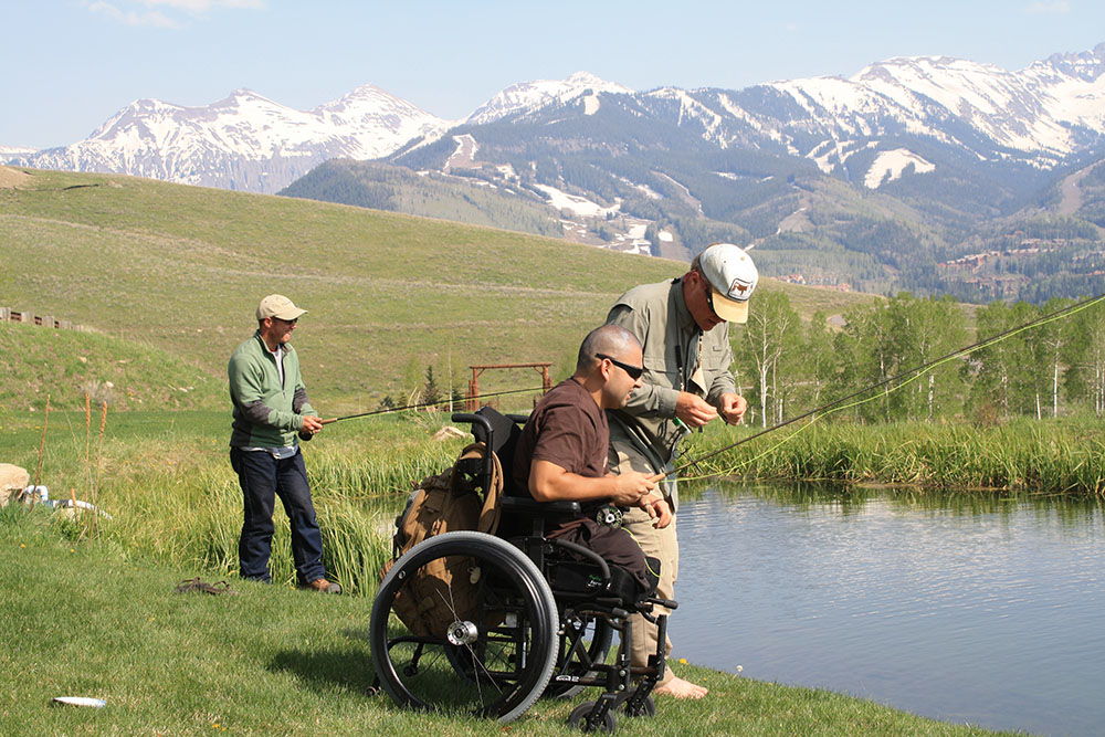 Person in fishing next to a pond sitting in a wheelchair.