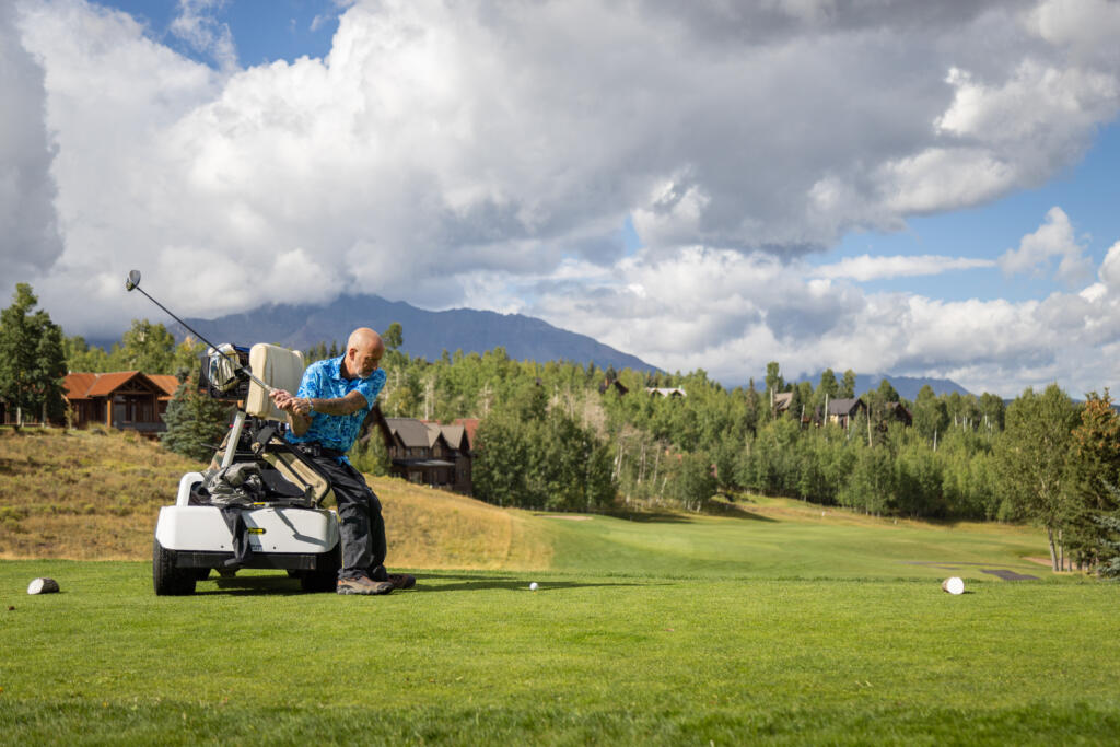 Athlete golfs at the Bob Miller Golf Tournament, using an assistive golf cart, supporting his back while he swings.
